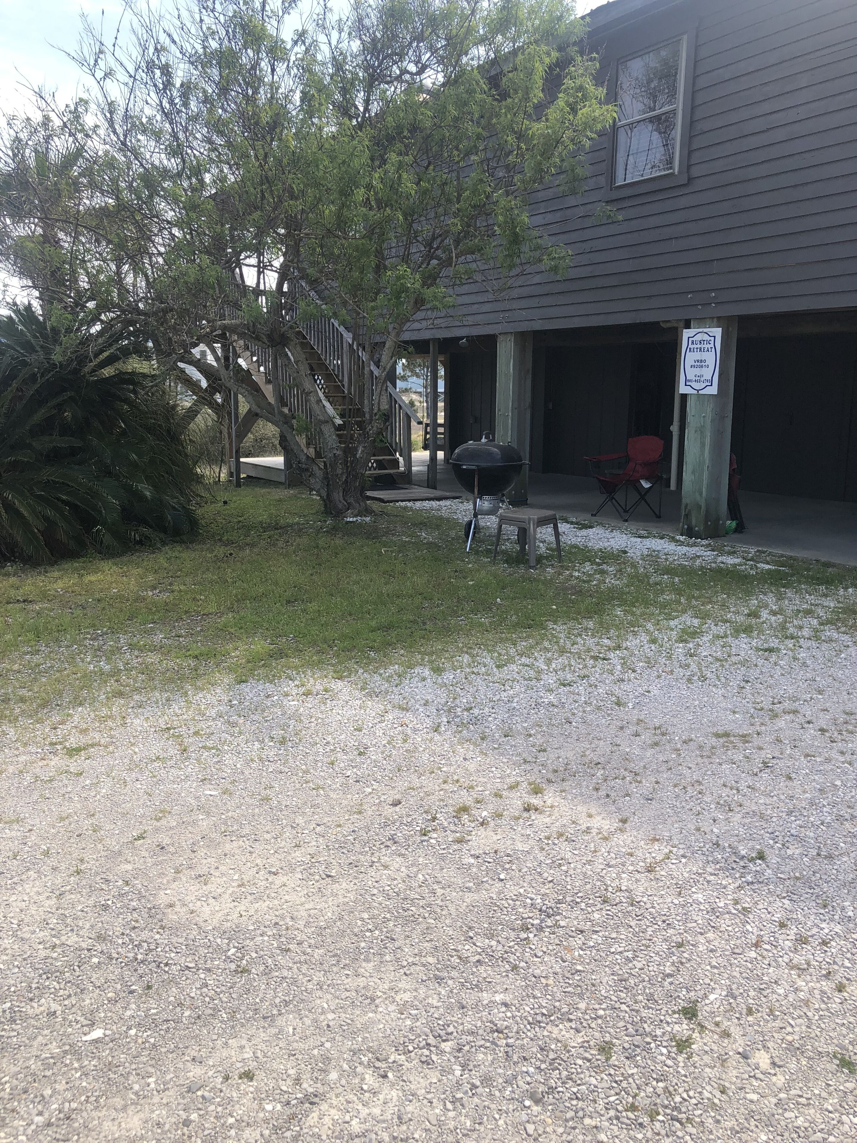 A rustic retreat with a covered outdoor area, a barbecue grill, and a gravel driveway.