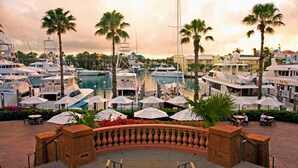 En lysthavn med flere sejlbåde i havnen, omgivet af palmer og et poolområde med parasoller.