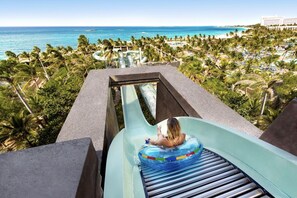 A person on a water slide with a view of a beach and palm trees. - Steps from Atlantis Waterpark + Passes for 10 Guests at Harborside Resort (Paradise Island)