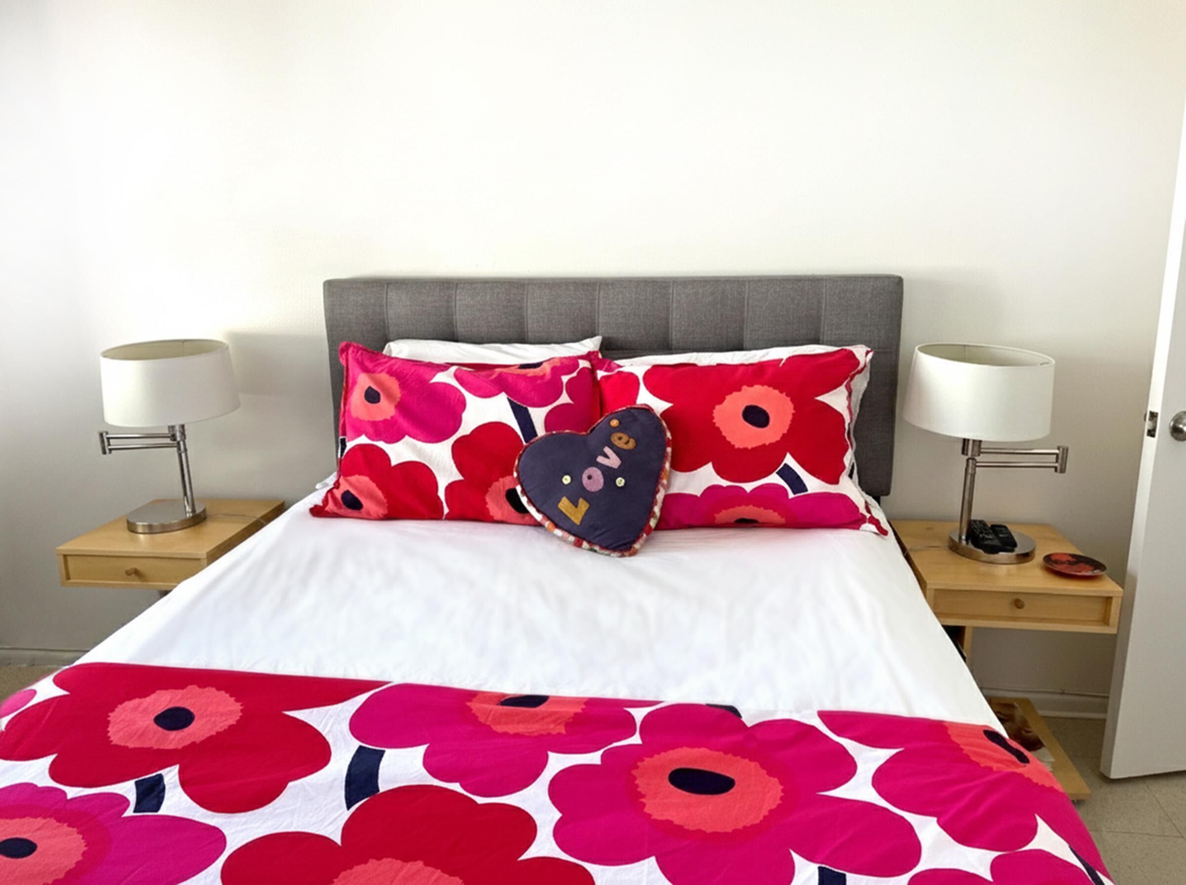 A bed with a floral bedspread, two bedside lamps, and a heart-shaped pillow.