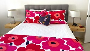 A bed with a floral bedspread, two bedside lamps, and a heart-shaped pillow. - The Getaway 1BR #1: Pool, Mountain View, Kids/Pets welcome (Desert Hot Springs)