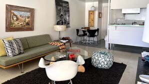 A modern living room with a green sofa, a glass coffee table, and a dining area with a black table and chairs. - The Getaway 1BR #1: Pool, Mountain View, Kids/Pets welcome (Desert Hot Springs)