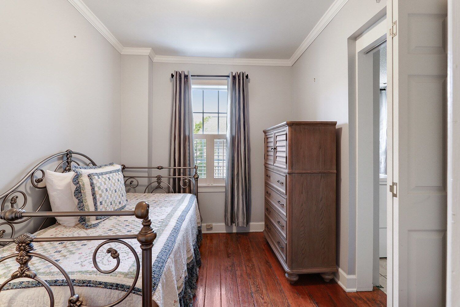 Une chambre à coucher avec un lit, une commode et une fenêtre avec des rideaux.