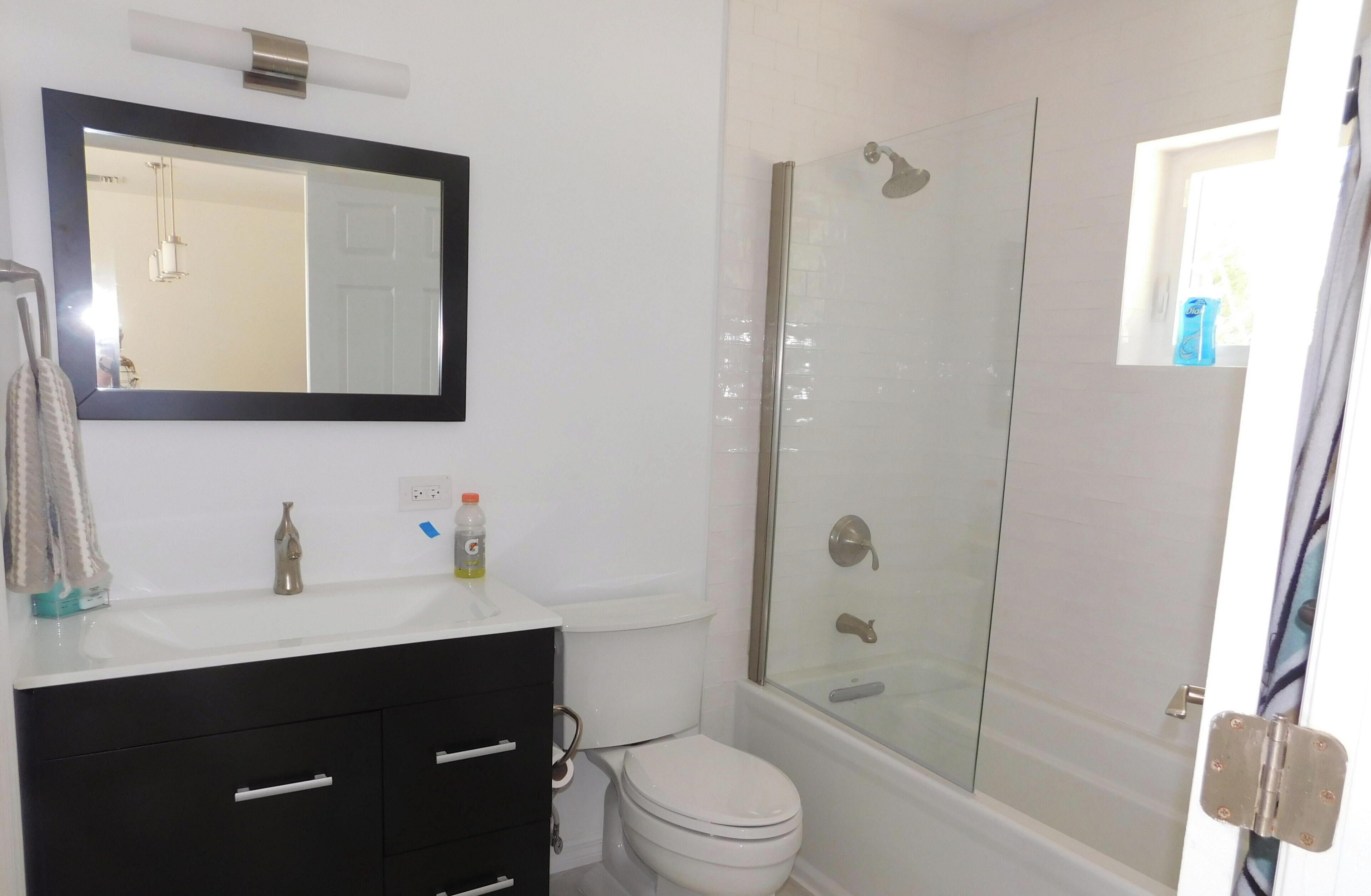 Une salle de bain avec un lavabo blanc, un meuble-lavabo noir, des toilettes et une douche à parois de verre.
