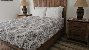 A bed with a patterned bedspread, wooden headboard, two bedside tables with lamps, and a small picture on the wall. - Base Camp / Bonanza (Thompson springs)