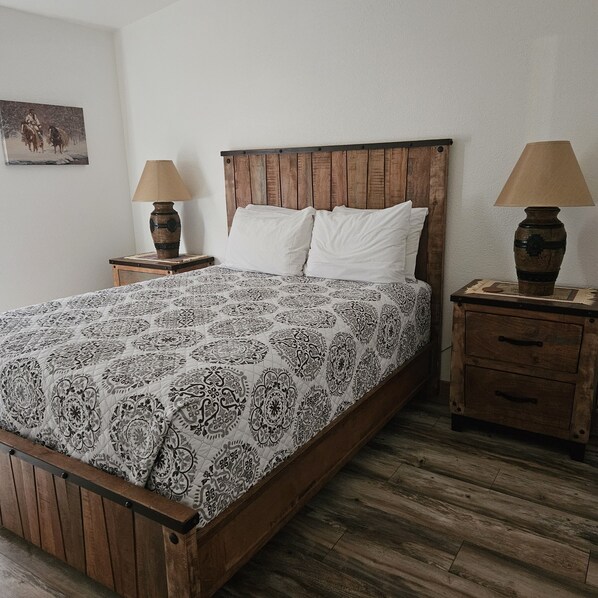 A bed with a patterned bedspread, wooden headboard, two bedside tables with lamps, and a small picture on the wall.
