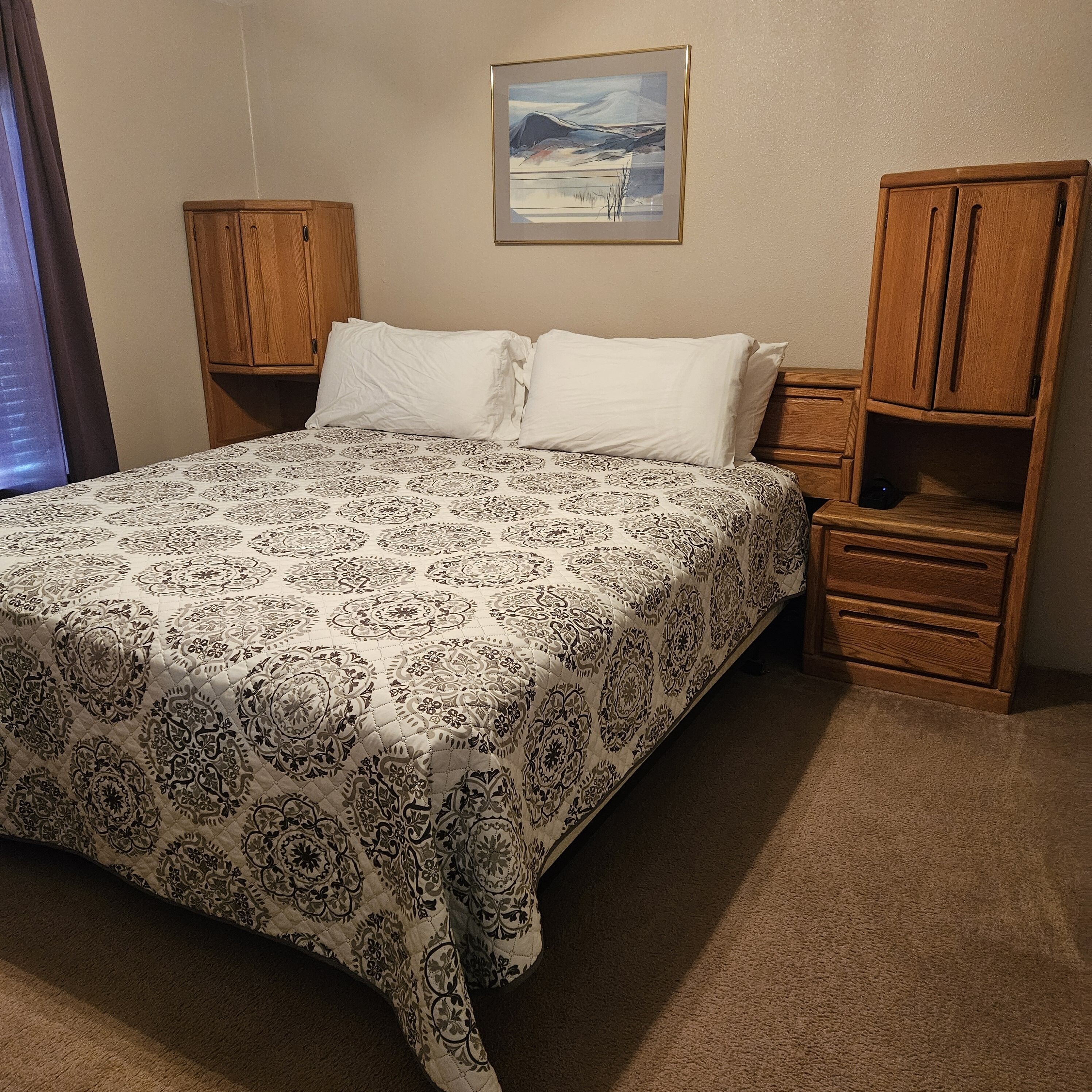 A neatly made bed with a patterned bedspread, wooden headboard, and nightstands with drawers.