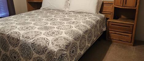 A neatly made bed with a patterned bedspread, wooden headboard, and nightstands with drawers.