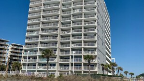 A multi-story hotel with balconies, located near a beach with a fence and palm trees. - Reduced Rates!!  A+ Spectacular Beach Front Condo! 1 BR 2 bath, sleeps up to 6. (Orange Beach)
