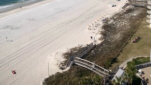 A beach with a clear sky, a sandy shore, and a few people walking. There is a wooden walkway leading to a building with a ramp. - Reduced Rates!!  A+ Spectacular Beach Front Condo! 1 BR 2 bath, sleeps up to 6. (Orange Beach)