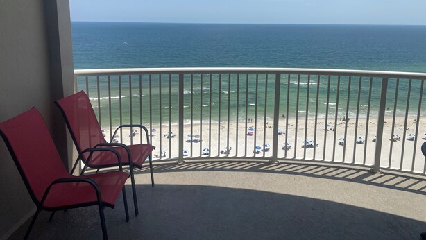 A balcony with red chairs overlooking a beach with umbrellas and people. - Reduced Rates!!  A+ Spectacular Beach Front Condo! 1 BR 2 bath, sleeps up to 6. (Orange Beach)