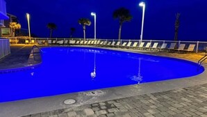 An outdoor swimming pool at night with a paved deck, lounge chairs, and palm trees. - Reduced Rates!!  A+ Spectacular Beach Front Condo! 1 BR 2 bath, sleeps up to 6. (Orange Beach)
