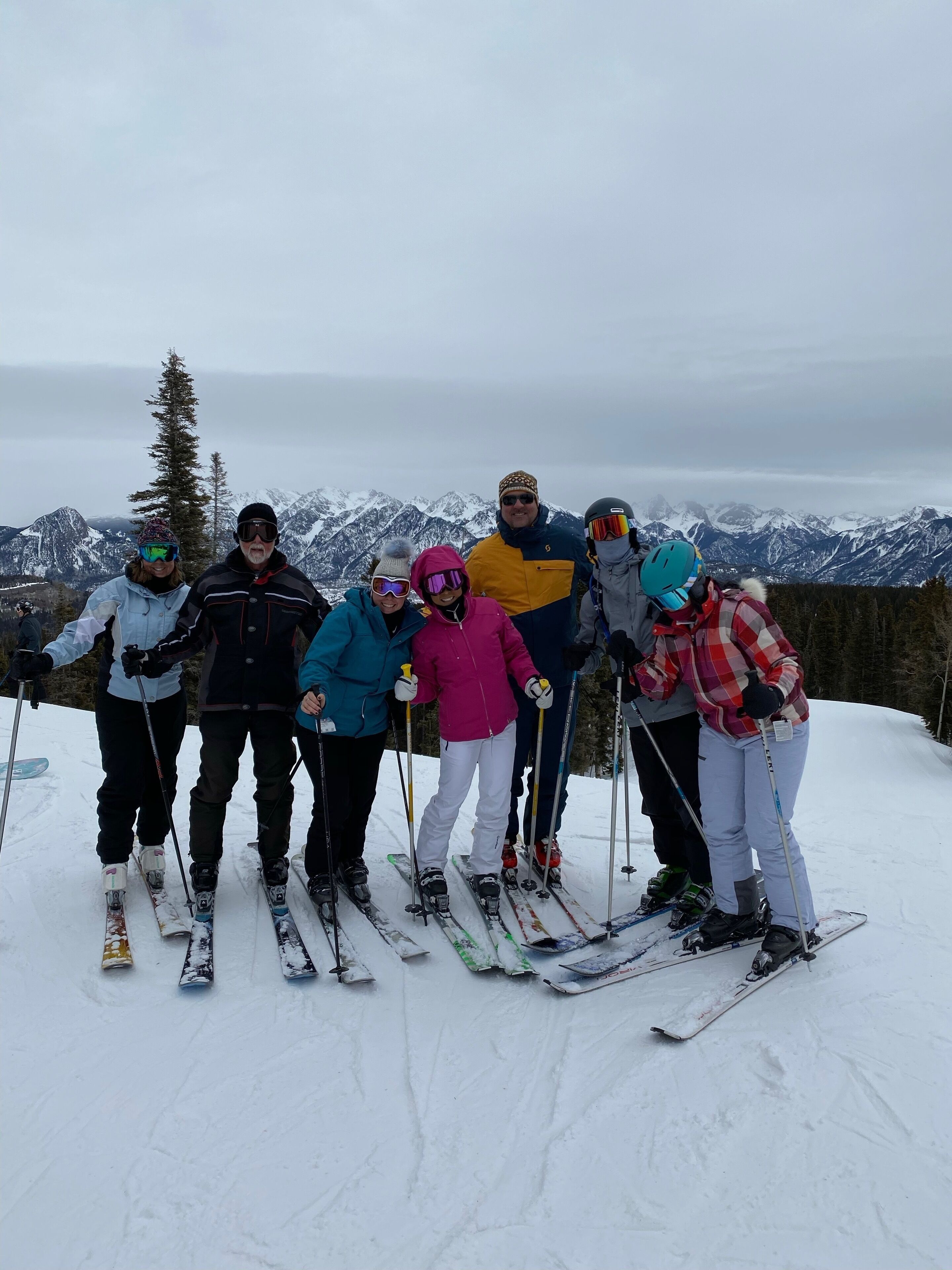 En grupp personer på skidor poserar på en snötäckt sluttning med ett berg i bakgrunden.