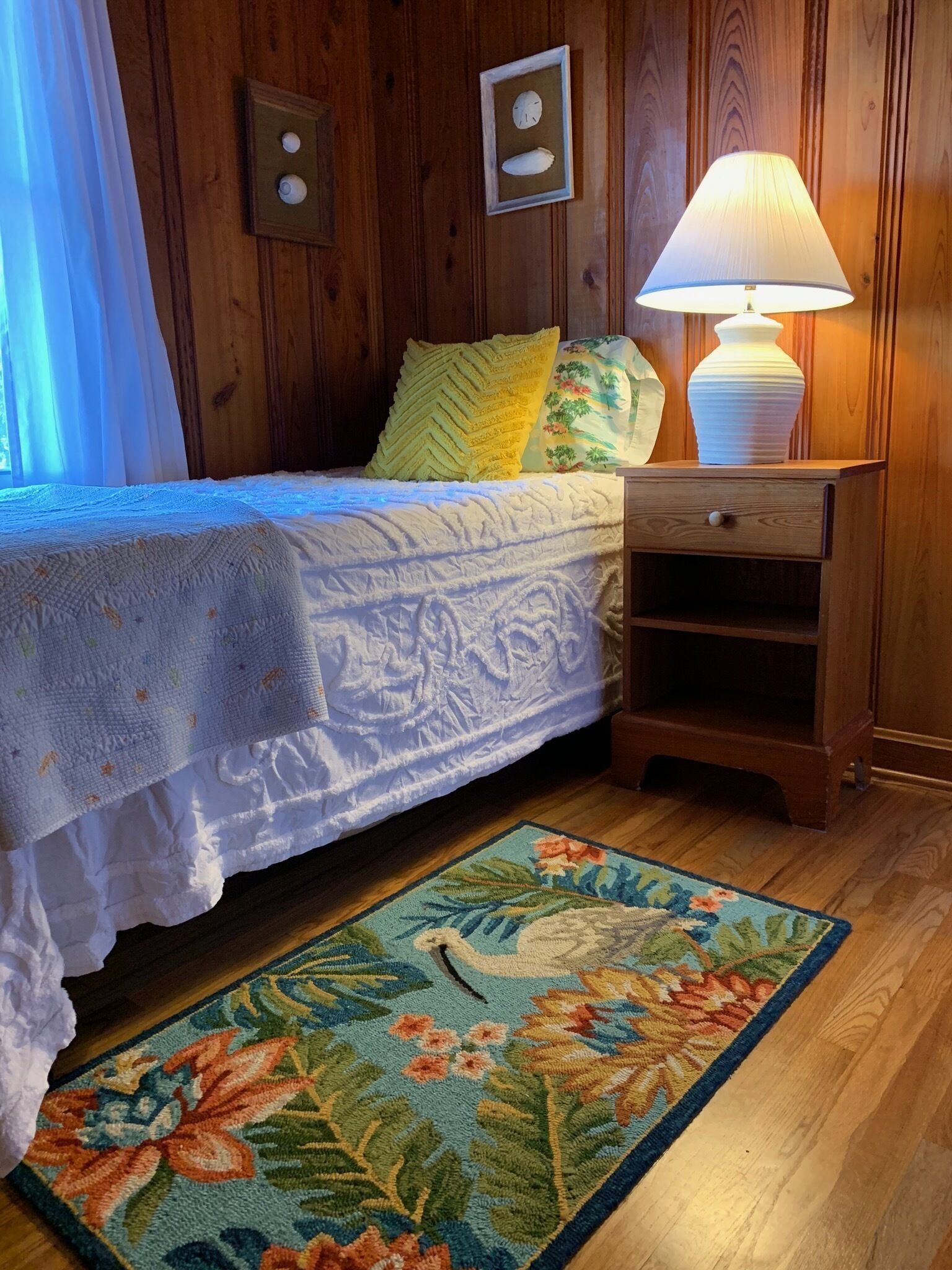 A bedroom with a bed, a nightstand, a lamp, a wall clock, and a floral rug.