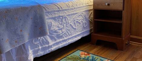 A bedroom with a bed, a nightstand, a lamp, a wall clock, and a floral rug.