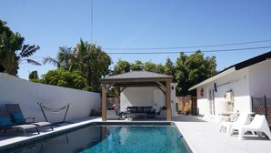 A swimming pool with lounge chairs and a covered seating area. - Large Resort House - Peloton, BBQ island, Firepit, Pool, Spa! (Anaheim)