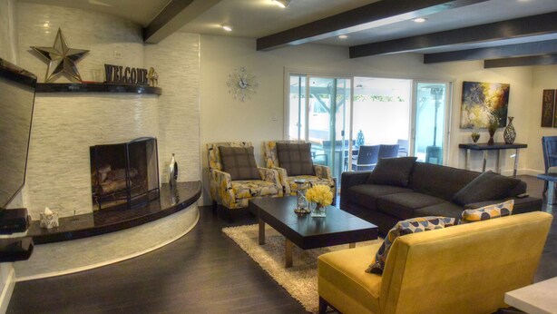 A modern living room with a fireplace, a sofa, a coffee table, and a chair. - Large Resort House - Peloton, BBQ island, Firepit, Pool, Spa! (Anaheim)