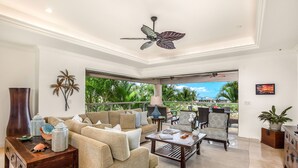 Ein geräumiges Wohnzimmer mit Deckenventilator, einer Couch, einem Couchtisch und Blick ins Freie.