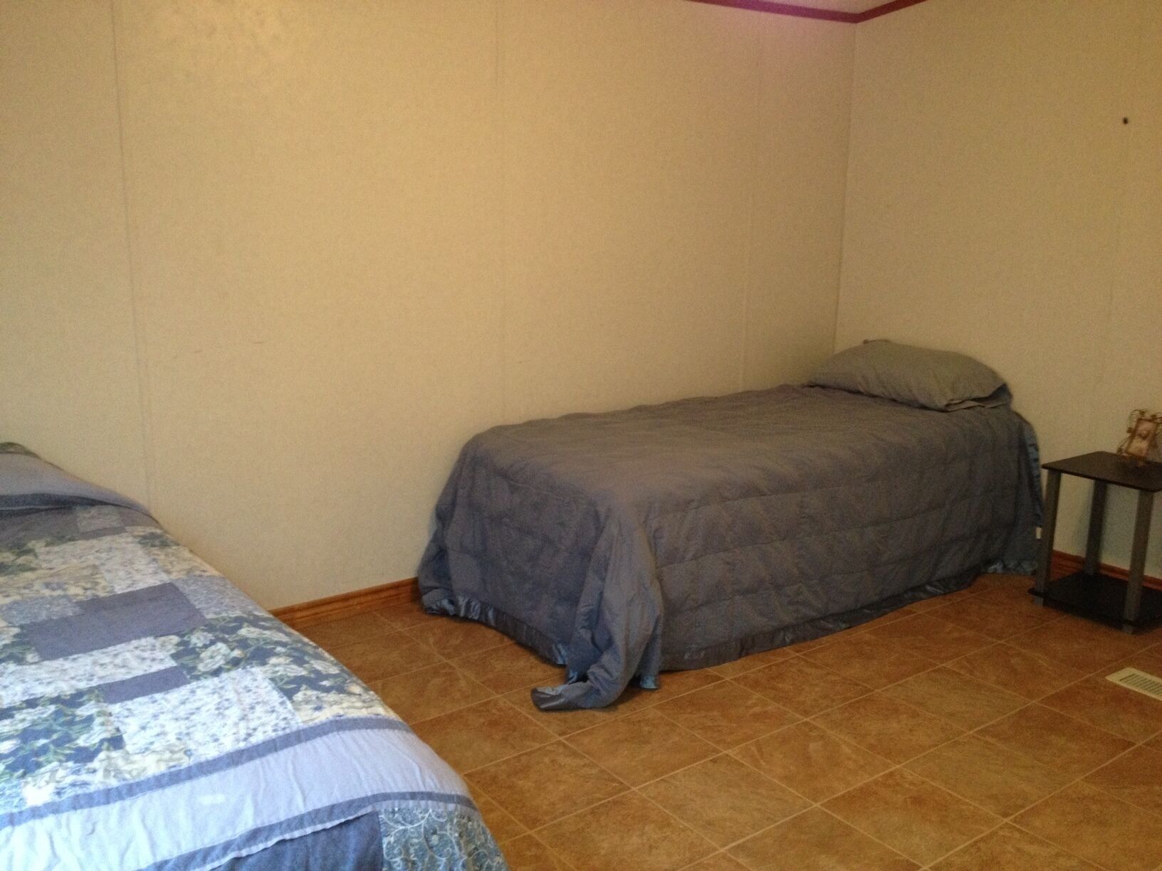 Een kleine kamer met een enkel bed, een effen muur en een betegelde vloer.