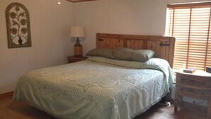 Quarto com cama, mesa de cabeceira, luminária e cômoda.