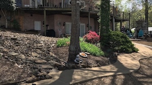 A two-story building with a stone retaining wall, a covered outdoor seating area, and a well-maintained garden with shrubs and a pathway. - Outdoor family time on the patio, at the pool-pool house, or on the boat dock! (Lexington)