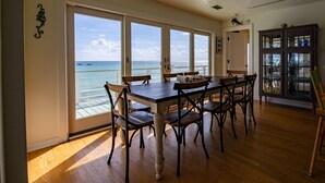 A dining area with a large table and chairs, a view of the ocean through large windows, and a cabinet with glass doors. - LABOR DAY SPECIALS ,BEACHFRONT, PRIVATE BEACH ON THE WATERFRONT, Bring your Dog (Anna Maria)