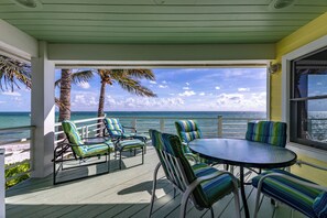 Un espace extérieur abrité, doté d’une table et de chaises, offrant une vue sur l’océan et bordé de palmiers.