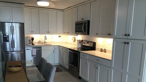 Cozinha moderna com armários brancos, eletrodomésticos de aço inoxidável e um espaço de refeições com banco e mesa.
