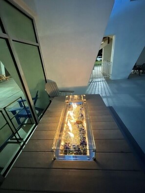 Un espace extérieur moderne, aménagé avec une table et des chaises à plateau en verre, un foyer et une vue sur les environs.