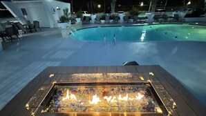 Área de piscina com lareira no primeiro plano e espreguiçadeiras ao redor.