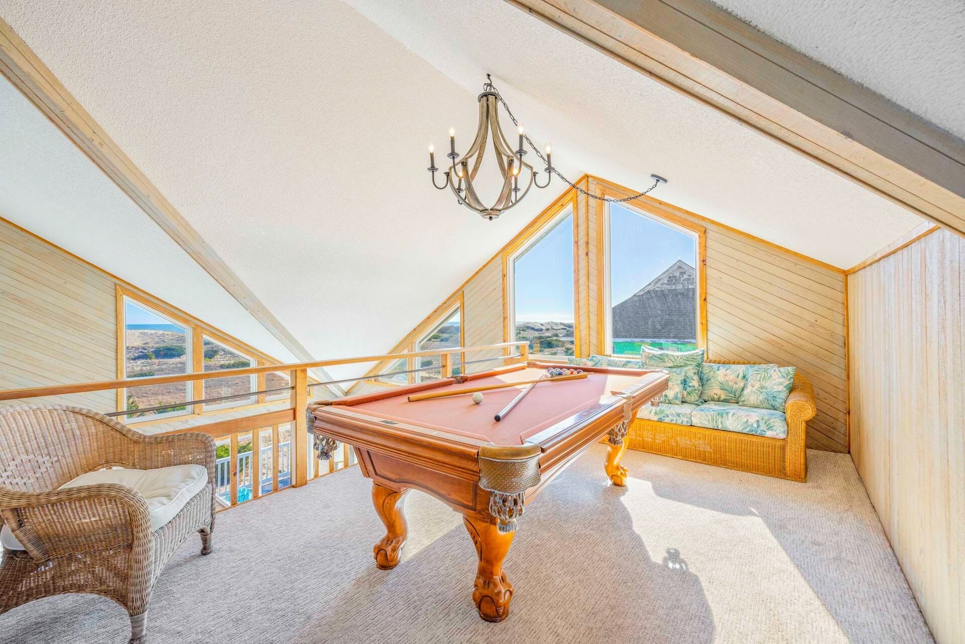 Una habitación acogedora con mesa de billar, sofá de mimbre y vistas al exterior a través de amplias ventanas.