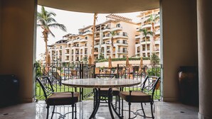 A round table with four chairs in a covered outdoor area, with a view of multi-story buildings and palm trees in the background.