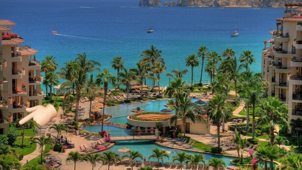 A resort with multiple swimming pools, palm trees, and a view of the ocean.
