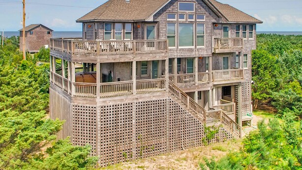 Une maison en bois à deux étages, dotée d’un balcon et d’une terrasse, entourée de verdure.