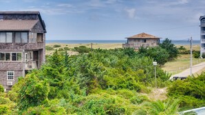 Une maison en bois à deux étages, dotée d’un balcon, entourée d’une végétation luxuriante et offrant une vue sur l’océan.