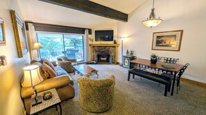 A living room with a fireplace, a sofa set, a dining table with chairs, and a television mounted on the wall.