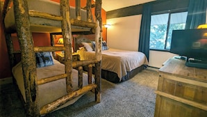 A rustic room with two bunk beds, a television on a wooden dresser, and a window with a view of trees. - Spacious Condo w/ FREE WiFi, Parking, Heated Pool, Hot Tubs, Skier Shuttles (Avon)