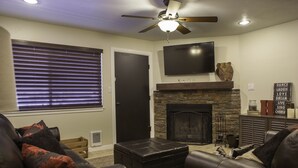 A living room with a fireplace, leather sofas, a television, and a ceiling fan.