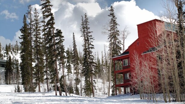 A red building surrounded by tall evergreen trees in a snowy landscape.