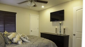 A bedroom with a bed, a dresser, a TV mounted on the wall, and a door.