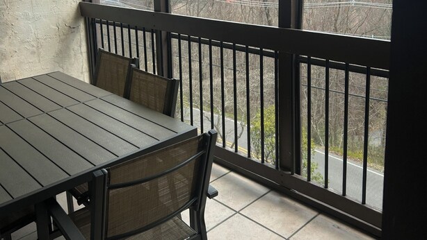 A balcony with a table and chairs, offering a view of mountains and a road.