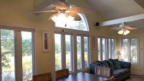 A dining area with a large table and chairs, a sofa with cushions, and a ceiling fan. - A Marsh View from this 3BR 2 Bath House (Tybee Island)