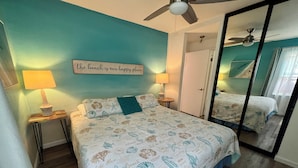 A bedroom with a bed, two bedside lamps, a ceiling fan, a mirror, and a sign on the wall.
