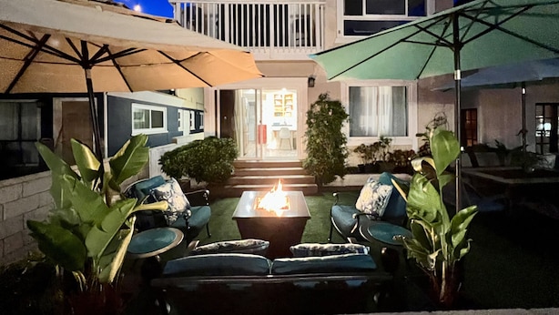 A two-story house with a balcony, outdoor seating area with chairs and a table, and a fire pit.