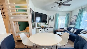 A living room with a round table, two blue armchairs, a sofa, a ceiling fan, and a staircase.