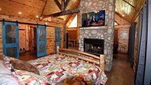 A cozy log cabin bedroom with a stone fireplace, a television mounted above it, and a bed with a colorful quilt. - Ole Blue (Broken Bow)