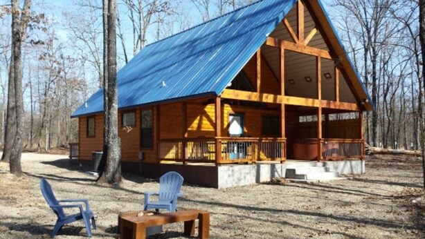 A wooden cabin with a blue metal roof, a porch, and a small table and chair set outside. - Ole Blue (Broken Bow)