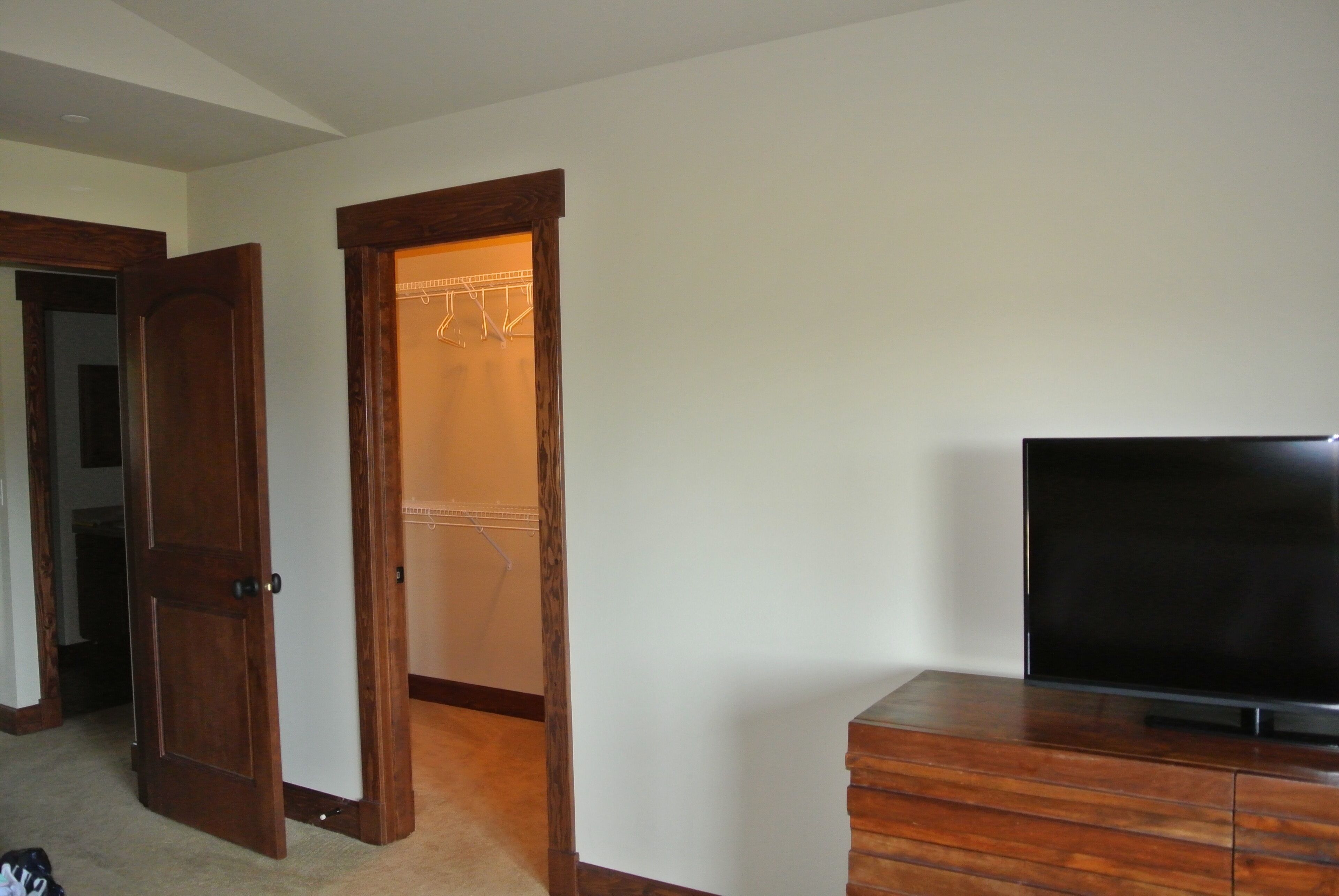 Ein Zimmer mit Holztür, einem Kleiderschrank mit Kleiderstange und einem Fernseher auf einem Holzgestell.