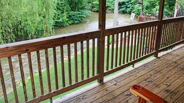 Een houten terras met een leuning met uitzicht op een rivier en begroeiing.