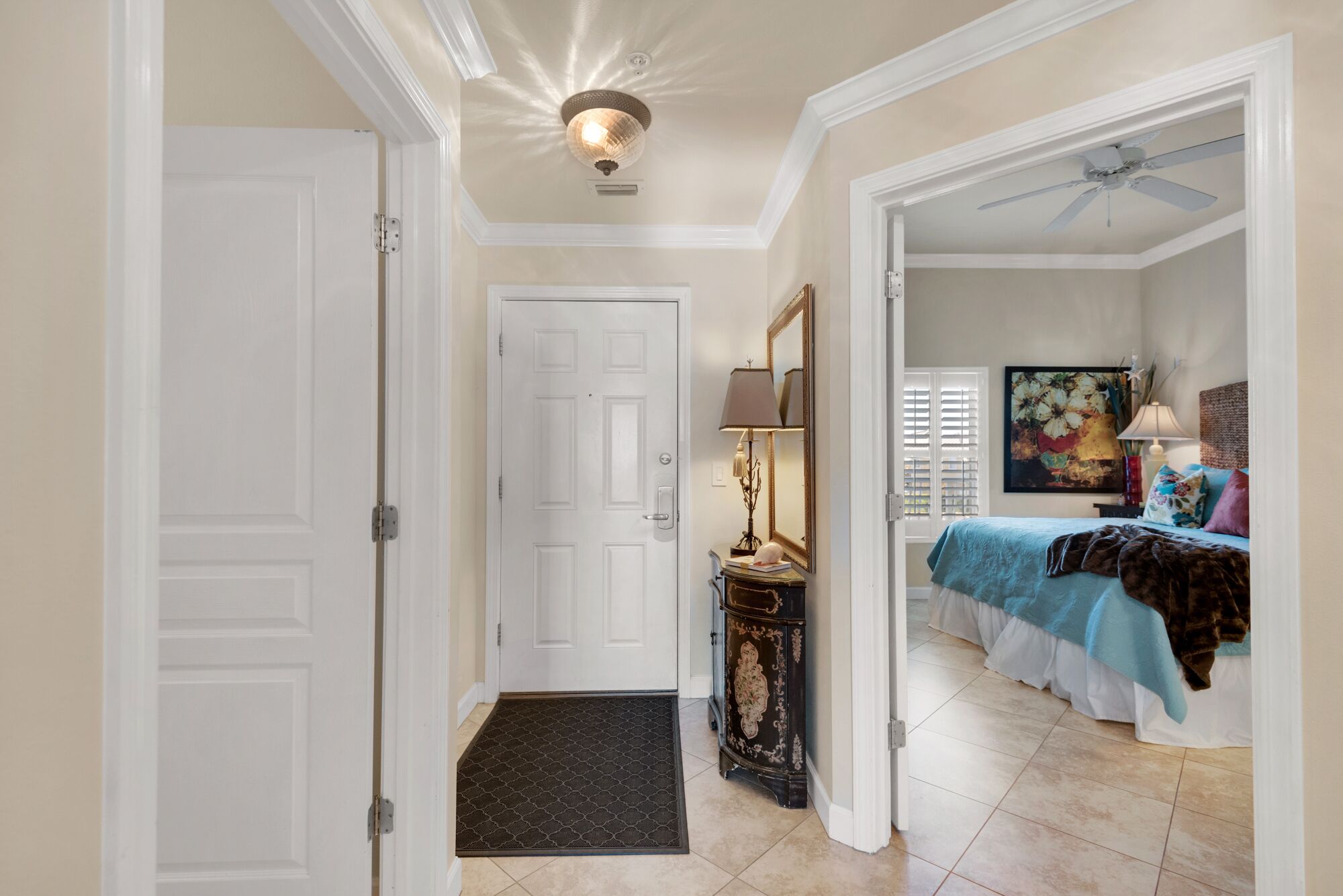 A hallway leading to a bedroom with a bed, a dresser, a mirror, and a ceiling fan.